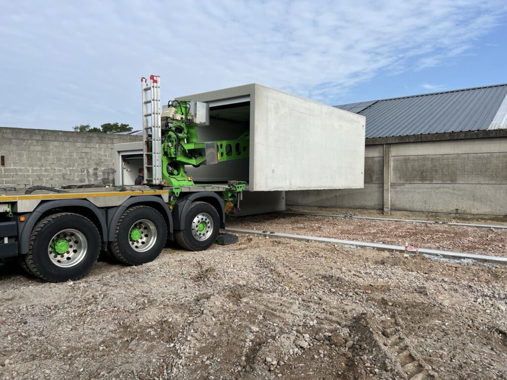 Betonal plaatsing prefab garage met vrachtwagen op verhard terrein met funderingsbalken in beton. Garage préfabriquée Betonal en béton sur un terrain avec des fondation placer par un camion.